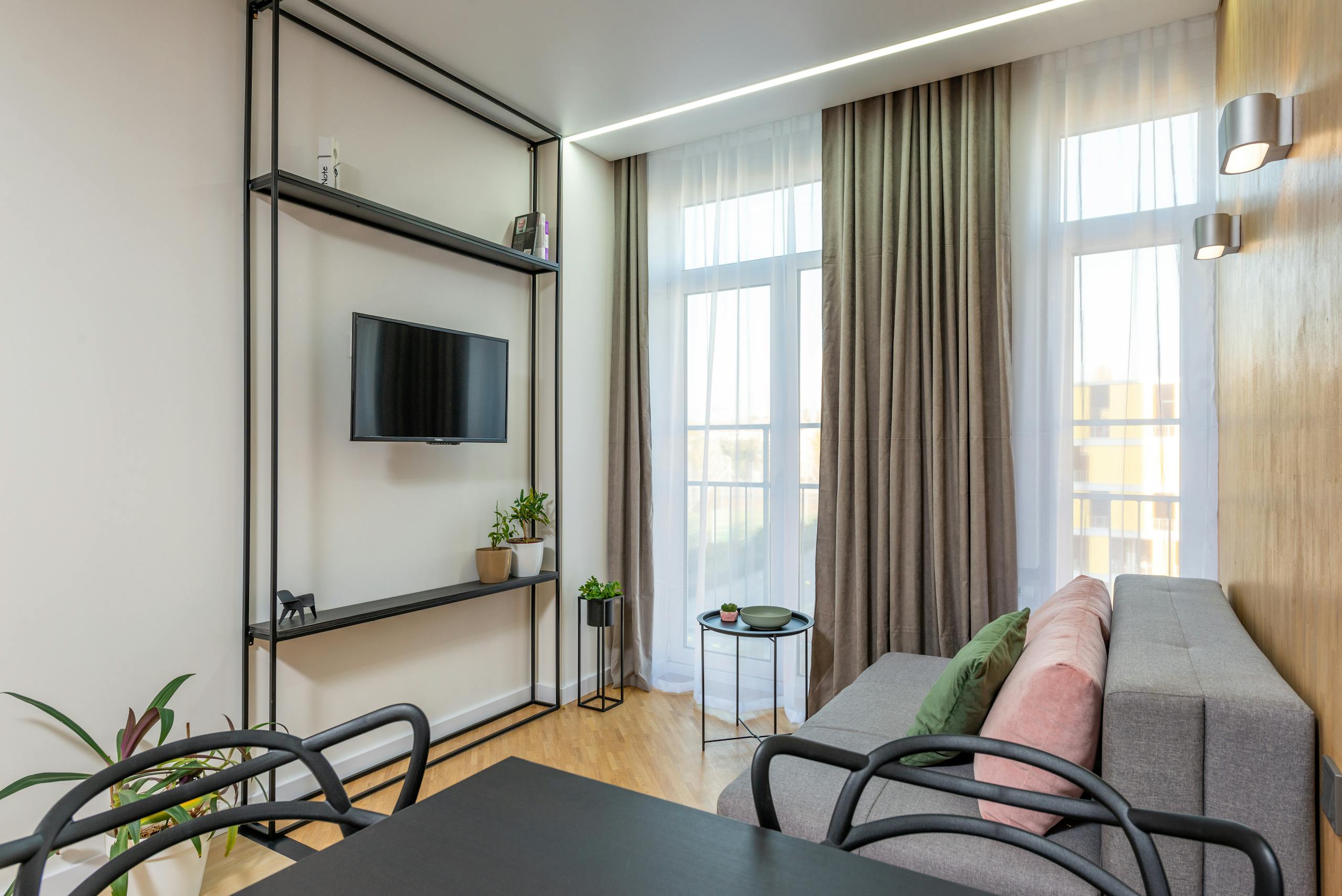 Stylish living room with contemporary decor, featuring a sofa, TV, plants, and elegant curtains.